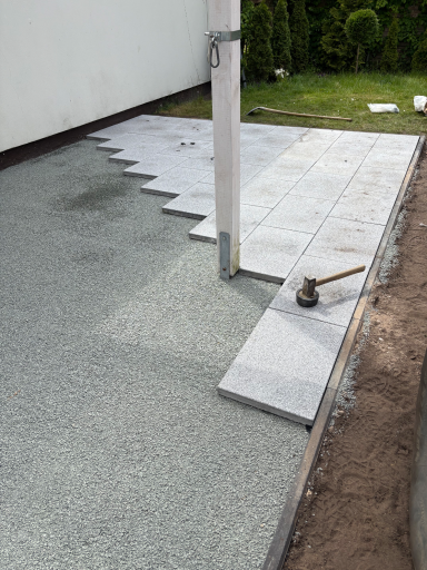 Bodenfläche mit verlegten Platten und einem Gummihammer auf frischem Beton.