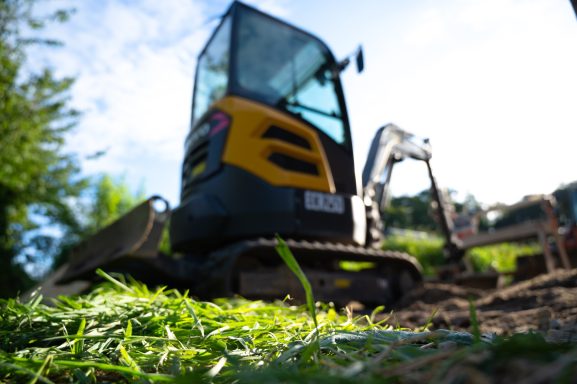 Kleinbagger auf einer Baustelle mit Gras im Vordergrund.