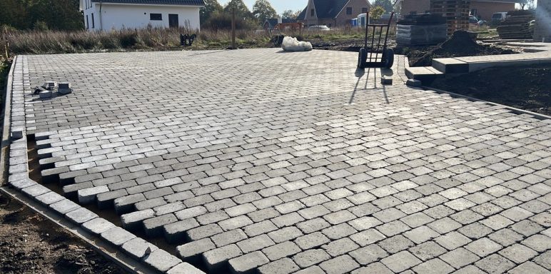 Gepflasterte Fläche mit unvollständigem Muster und Baustellenutensilien im Hintergrund.