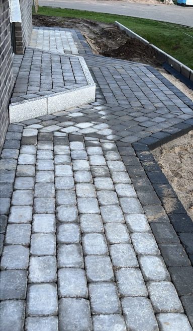 Ein gepflasterter Weg mit hellen Steinen in einem rechteckigen Muster.