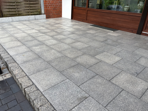 Gepflasterte Fläche mit quadratischen Steinplatten in verschiedenen Grautönen.